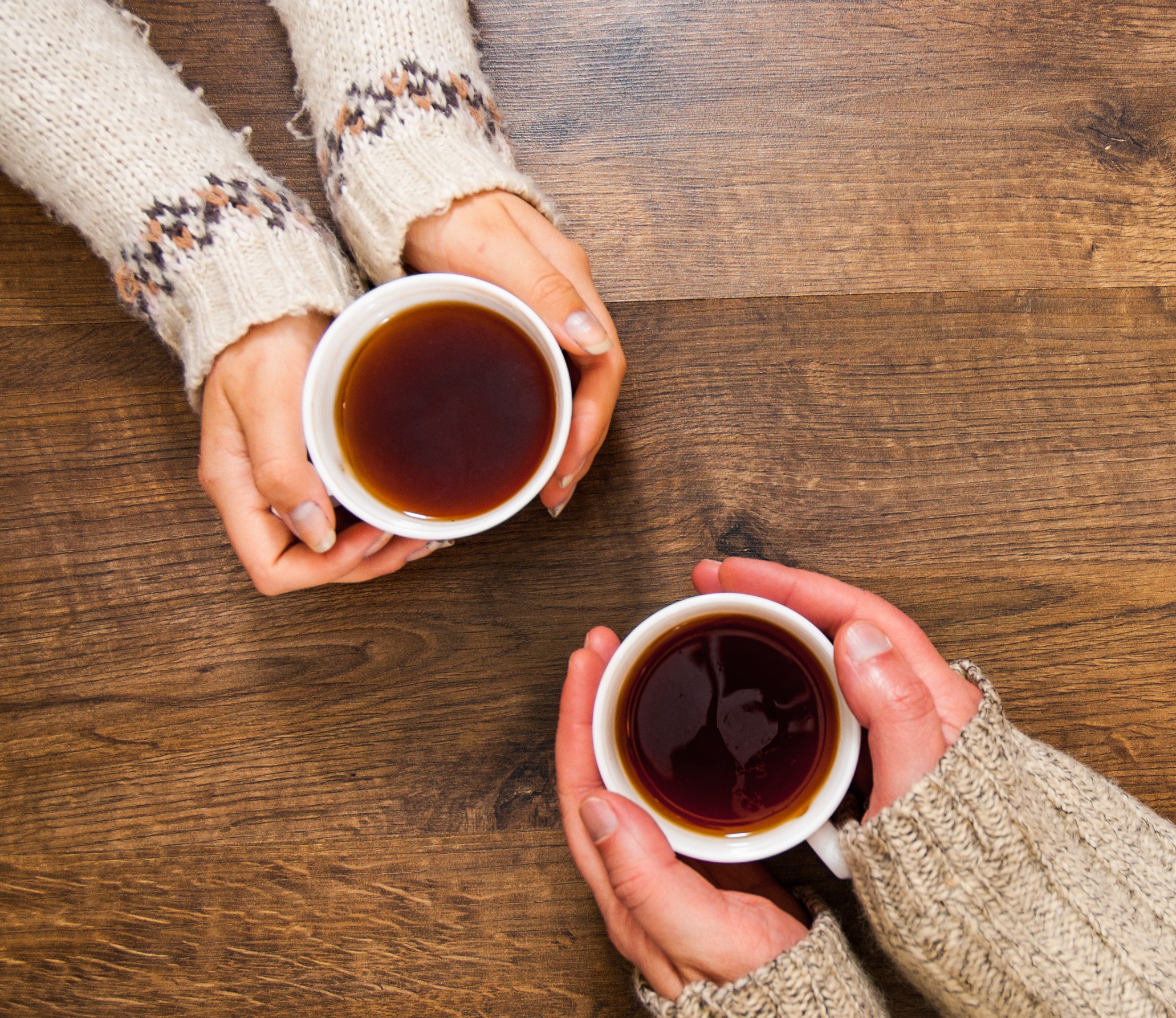 Two people sharing mugs of coffee over a wooden table